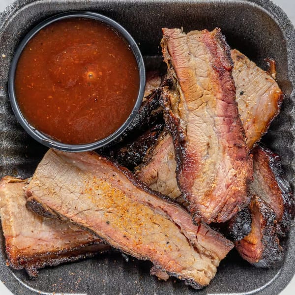 Alabama Que's BBQ brisket slices with a side of barbecue sauce in a black container.