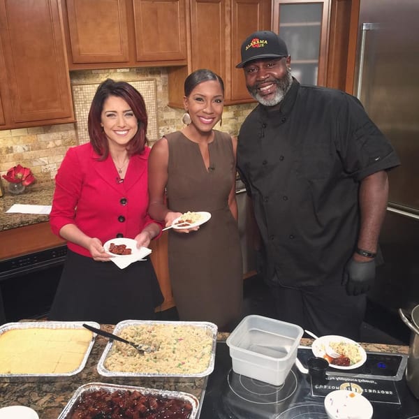 Two women and a man in a chef's hat and Alabama Que shirt pose with BBQ dishes.