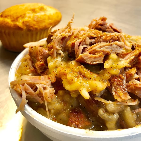 A white bowl of Alabama Que's BBQ stew with pulled pork and mac and cheese, with a cornbread muffin.