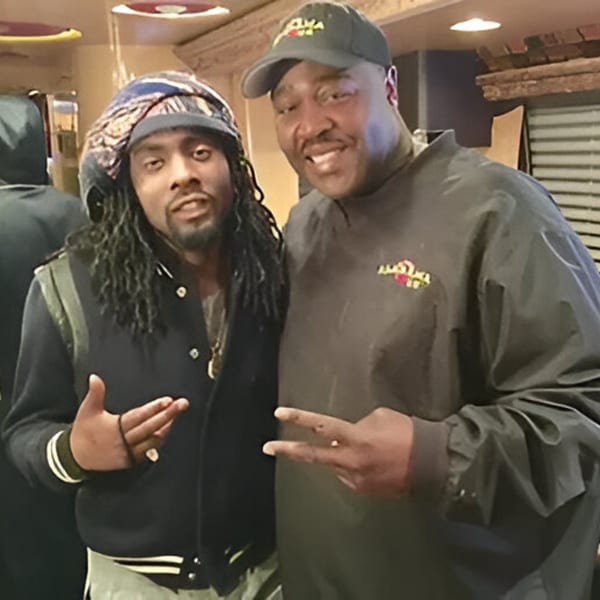 Two men, one in an Alabama Que hat, posing and smiling for the camera.