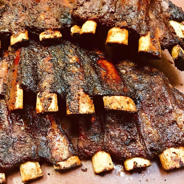 Close-up of several racks of Alabama Que's dark, smoky, barbecued ribs with visible bones.