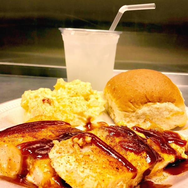 Alabama Que's BBQ chicken with potato salad, a dinner roll, and a drink.