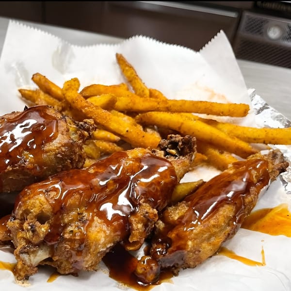 Alabama Que's BBQ chicken wings with a glossy sauce and a side of seasoned fries.