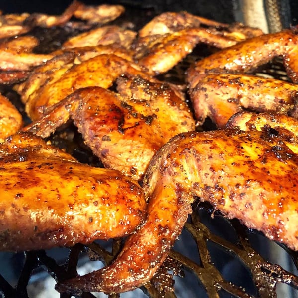 Close-up of golden-brown, glazed BBQ chicken wings cooking on a grill at Alabama Que.